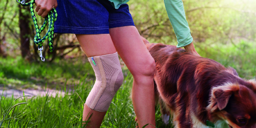 Μια γυναίκα που φορά ένα προϊόν υποστήριξης γονάτων βγάζει τον σκύλο της έξω Μια γυναίκα που φορά ένα προϊόν υποστήριξης γονάτων βγάζει τον σκύλο της έξω